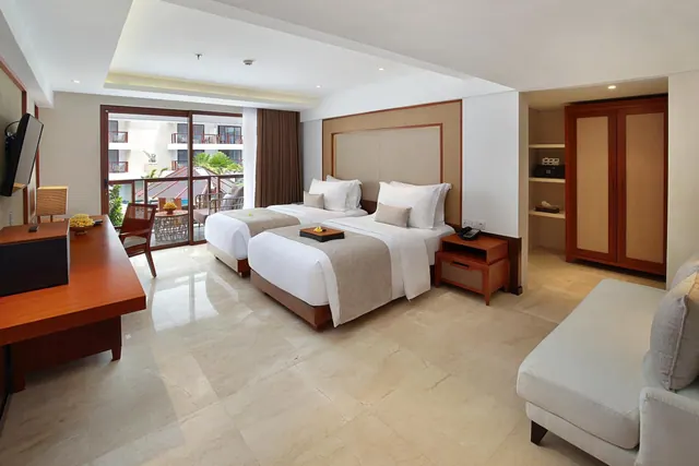 A bedroom with two beds, a wooden desk, a wardrobe, a white sofa, and sliding glass doors opening onto a balcony.