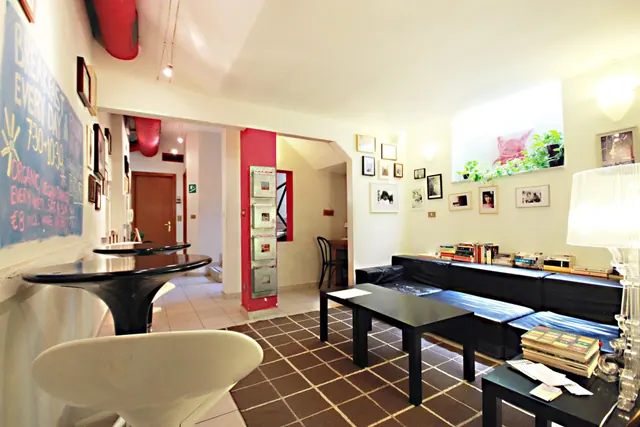 A lounge area with a black sofa, low coffee tables, framed photographs on the wall, and a chalkboard advertising breakfast every day.