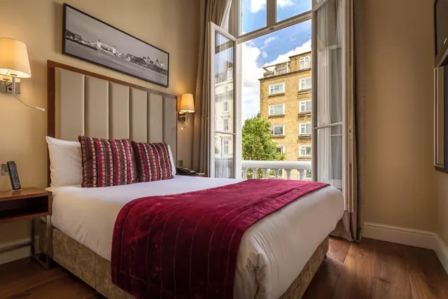 A double bed with a red throw and striped cushions sits in a bedroom with open French doors onto a small balcony.