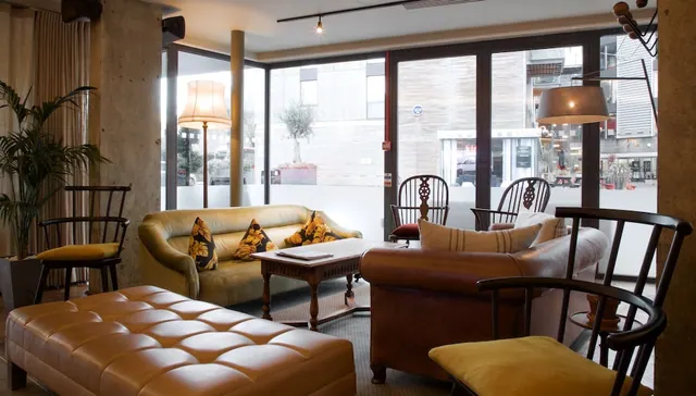 A lounge seating area with leather sofas, armchairs and a tufted leather ottoman, with floor-to-ceiling windows onto a street.