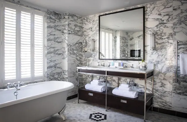 A bathroom with a freestanding clawfoot bathtub, a double vanity with folded white towels below it, and marble-clad walls.