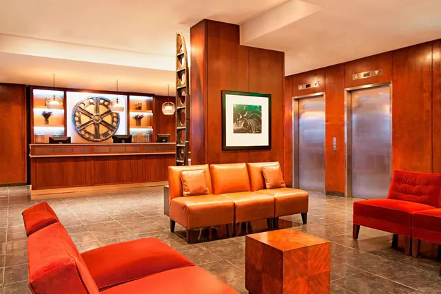 A lobby with a wood-paneled reception desk, leather and velvet armchairs, a wooden cube table and two elevators.