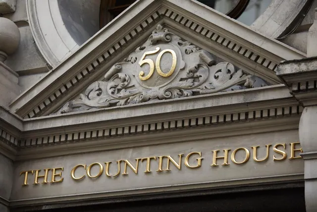 Close view of an ornate stone pediment with a gold number 50 and gold lettering reading THE COUNTING HOUSE on the building facade.