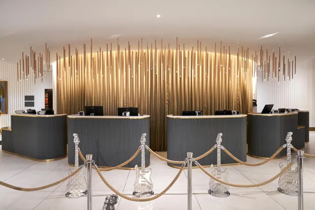 A reception area with curved grey front desks and monitors, a gold backdrop of hanging copper rods, and crystal guitar sculptures behind rope barriers.