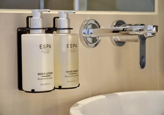 Two wall-mounted ESPA body lotion and hand wash dispensers sit beside a chrome wall tap above a white basin.