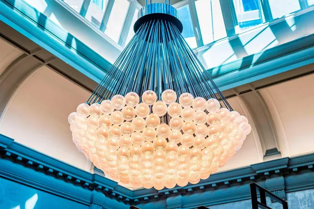 A large glass-globe chandelier hangs beneath a skylight in a high arched ceiling with blue-painted cornices.