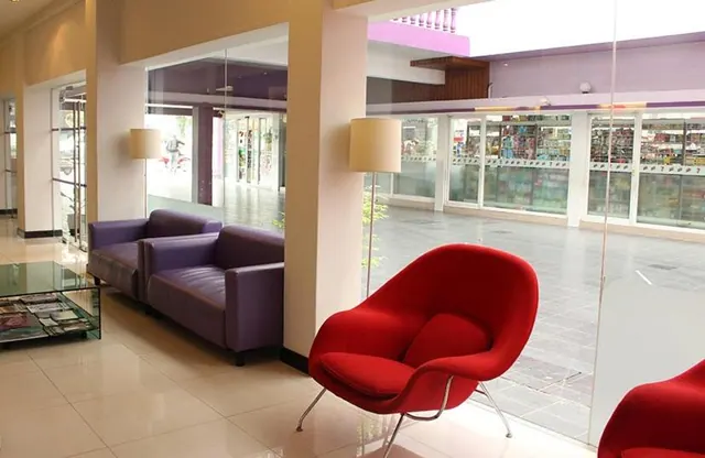 A lounge seating area with red armchairs, purple sofas and a glass coffee table beside floor-to-ceiling windows that look onto a shopping walkway outside.