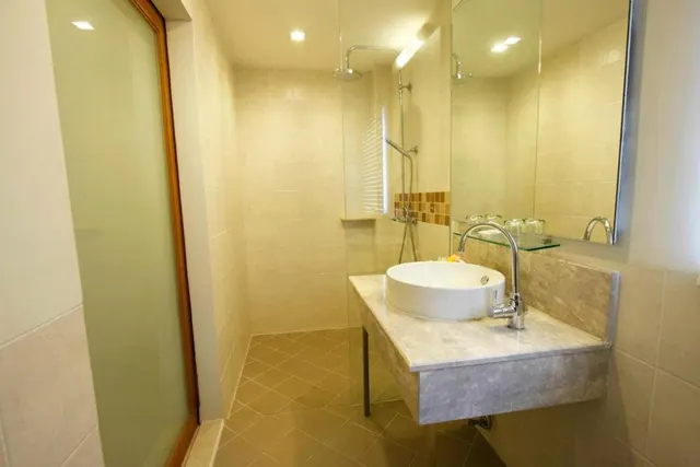 A bathroom with a round white vessel sink on a marble counter, a chrome mixer tap, a mirror, and a walk-in shower behind a glass partition.
