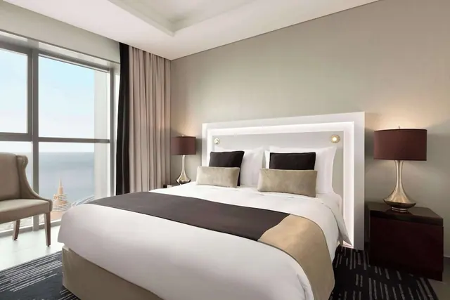 A bedroom with a king bed, an armchair and floor-to-ceiling windows looking out over the sea.