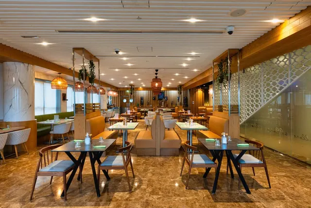 A restaurant dining room with dark tables, wooden chairs, booth seating and woven pendant lamps under a slatted ceiling.