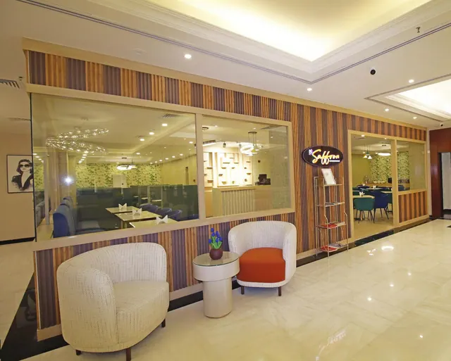 A lobby seating area with two cream armchairs and a side table with a flower pot, beside a glass partition leading to the Saffron restaurant.