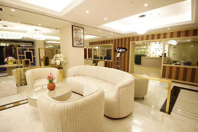A lobby seating area with a cream curved sofa, armchairs, a glass coffee table with tulips, and a wood-slatted wall with a Saffron sign.
