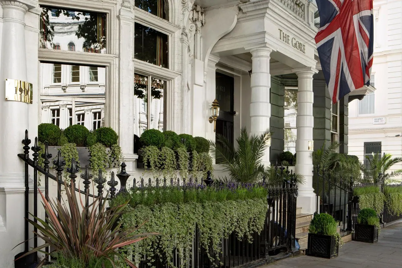 The white facade and columned entrance of The Gore hotel, with a Union Jack flag, black iron railings and clipped topiary in planters.