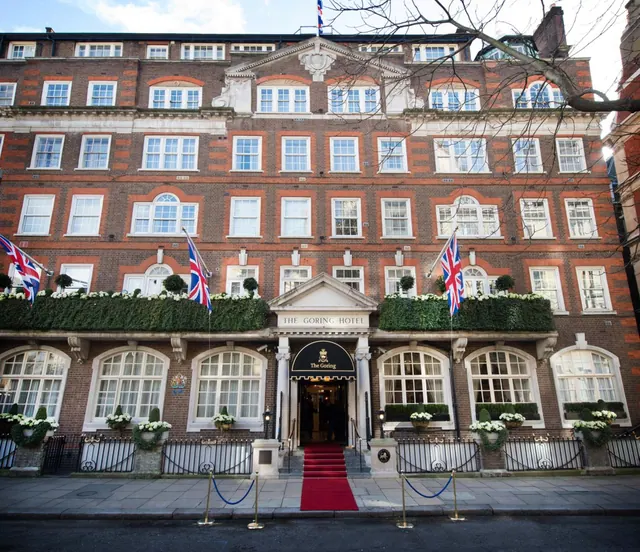 The front facade of The Goring Hotel with Union flags, a red carpet leading to the entrance and brass barrier posts on the pavement.