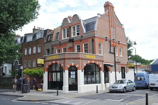 Exterior of a brick corner building with a sign reading The Grange, with a few people on the pavement and parked cars on the street.