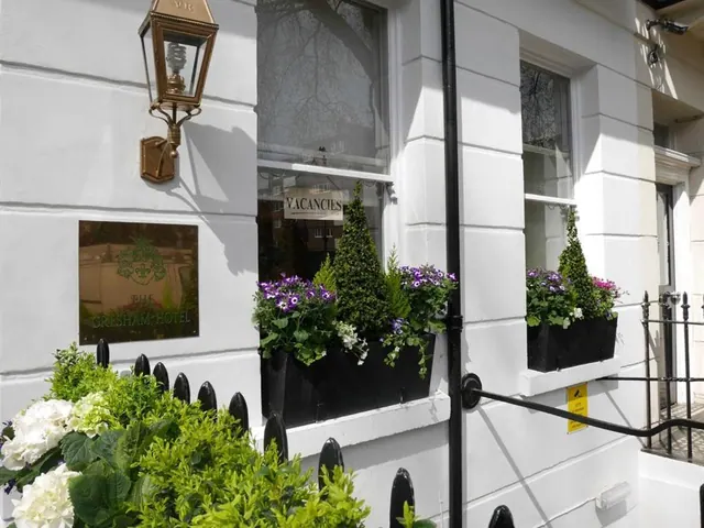 The white facade of The Gresham Hotel shows a brass wall lantern, a name plaque, a Vacancies sign in a window, and flower boxes under the windows, with black railings in front.