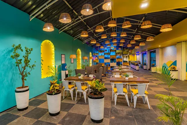 A spacious restaurant dining area has wooden tables, metal chairs, lounge seating, potted plants and woven pendant lights.