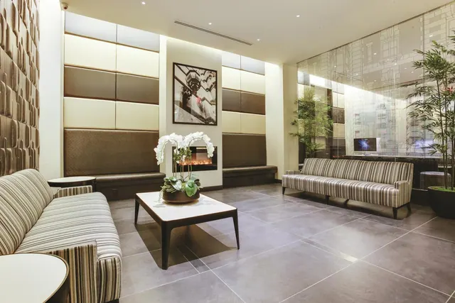 A lobby seating area with striped sofas, a low coffee table holding a white orchid, a lit fireplace, and padded wall panels.