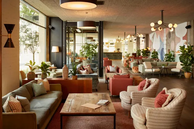 A lounge with grey and cream sofas, armchairs and a wooden coffee table, with large windows on the left and a bar in the background.