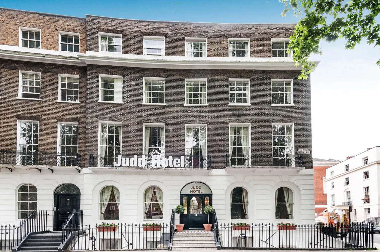 Front exterior of the Judd Hotel, a brick building with white painted ground floor, arched windows, iron railings and a black entrance door under a sign reading Judd Hotel.