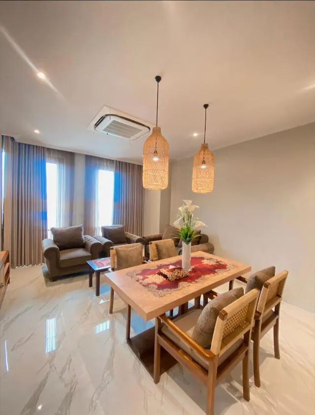 A living and dining area with a marble floor, a wooden dining table set for four, a sofa seating area, rattan pendant lights and a ceiling-mounted air conditioning unit.