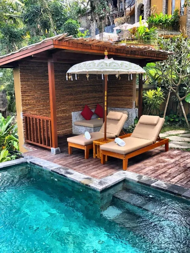 A small private swimming pool with a wooden deck, two sun loungers and a shaded gazebo with a patterned umbrella.