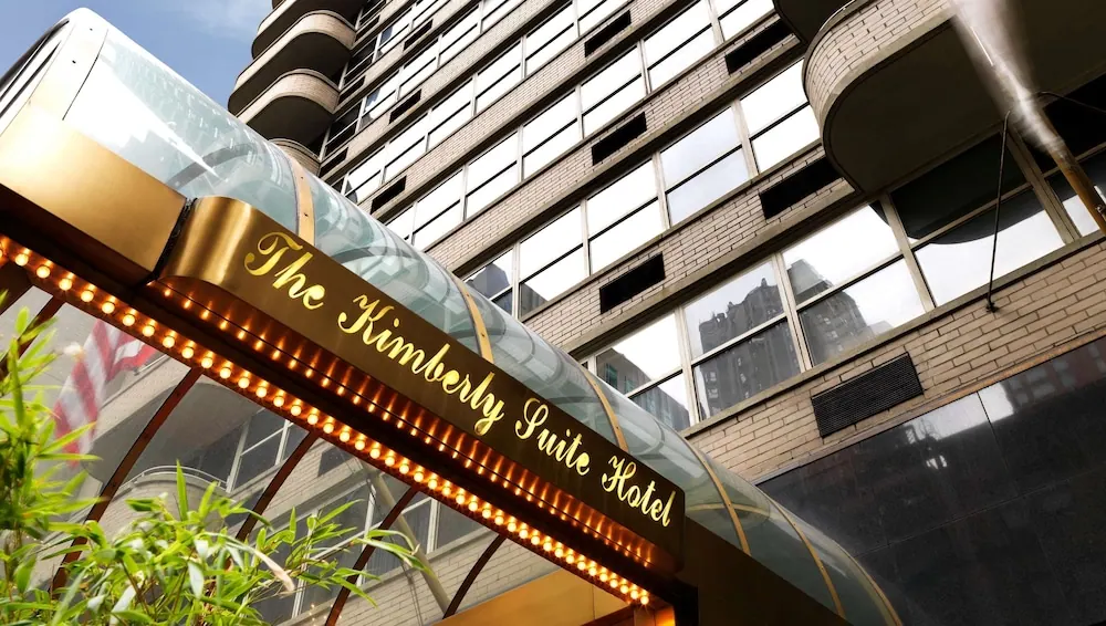 Looking up at the illuminated entrance canopy and brick facade of The Kimberly Suite Hotel.