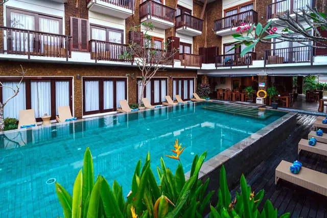 An outdoor swimming pool with sun loungers and rolled blue towels, surrounded by a multi-storey building with balconies.