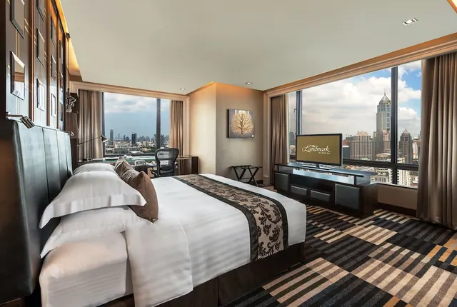 A king bed faces a television and a wall of windows with a city skyline view in a hotel bedroom.