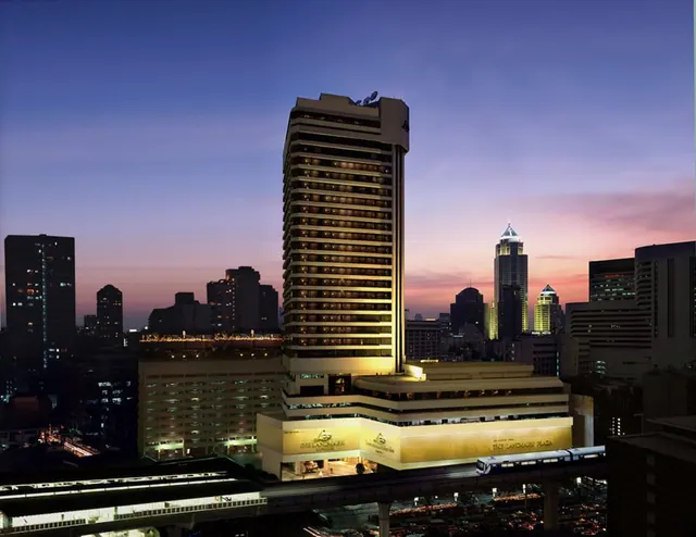 Exterior view of The Landmark hotel tower at dusk, with illuminated lower-level signage and city buildings behind it.