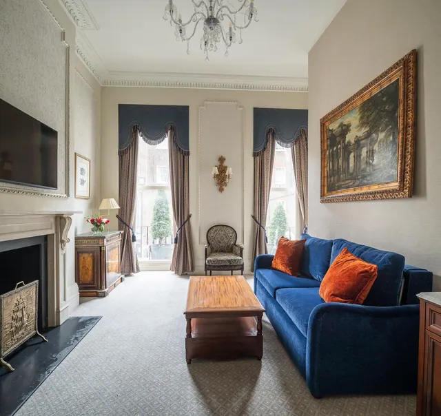 A living room with a blue sofa, orange cushions, a wooden coffee table, a fireplace, a wall-mounted television and a large framed painting.