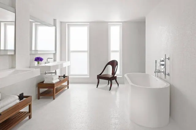 A white bathroom with a freestanding bathtub, a double vanity with towels on wooden shelves, and a dark wooden chair near the windows.