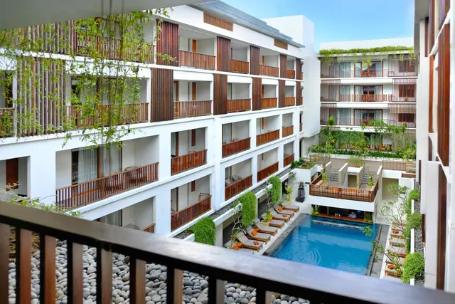 Looking down from a balcony onto a courtyard pool with sun loungers, surrounded by white multi-storey rooms with timber balconies and a pebble garden bed.