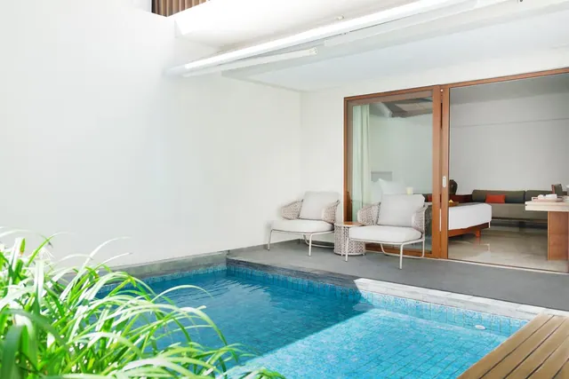 A small private pool on a grey terrace beside a glass sliding door, with white lounge chairs and a bedroom visible inside.