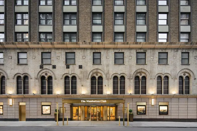 The front facade of The Manhattan Club at dusk, with arched windows and a gold-trimmed entrance canopy.