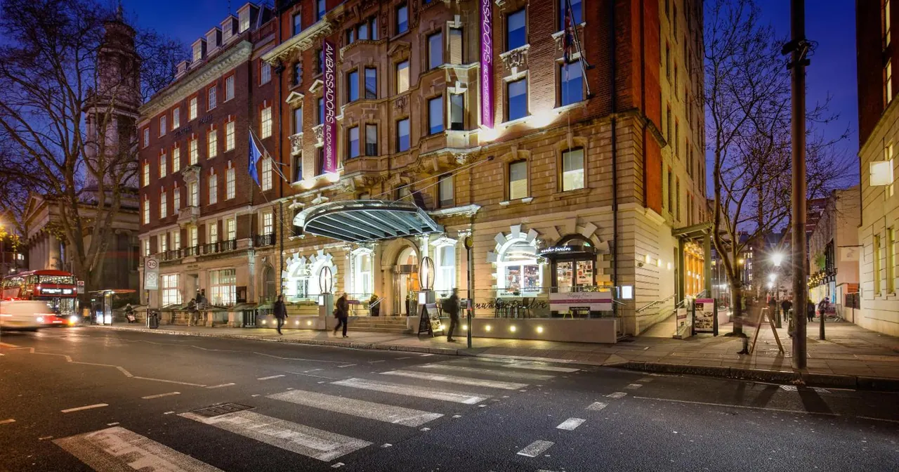 Exterior of a multi-storey brick and stone hotel building at dusk, with a glass canopy over the entrance and a zebra crossing in the street in front.