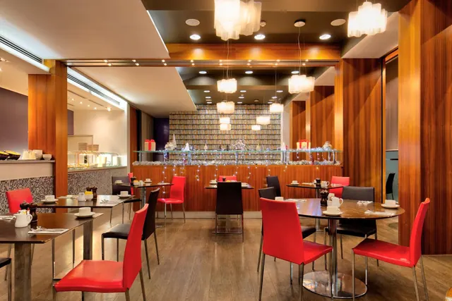 A dining room with red leather chairs, dark wood tables and wood-panelled walls, with a buffet counter on the left and a bar with glassware and pendant lights at the back.