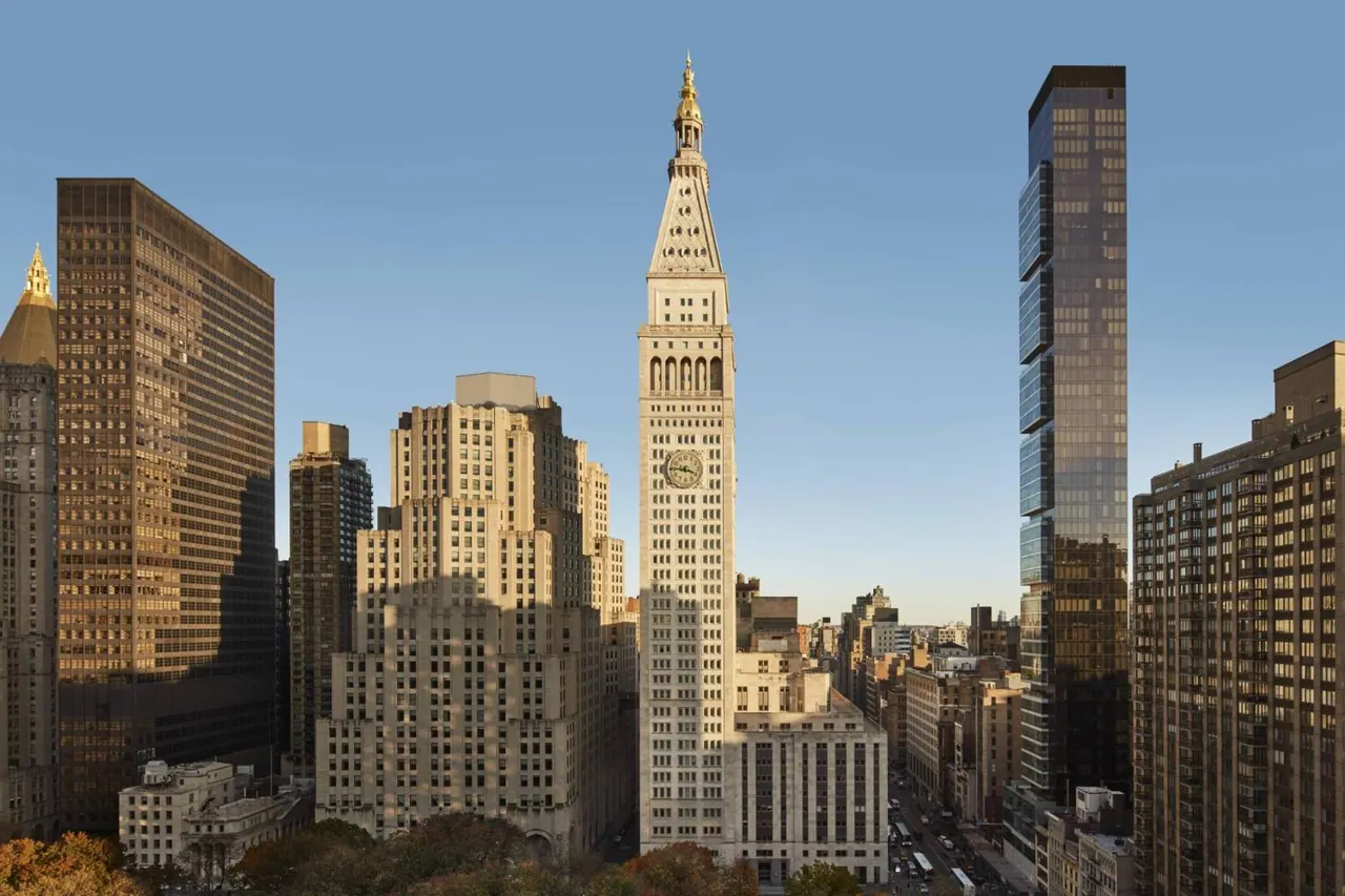 A wide view over a Manhattan skyline with the clock-topped MetLife Building tower in the centre, flanked by office and apartment towers and trees in the foreground.
