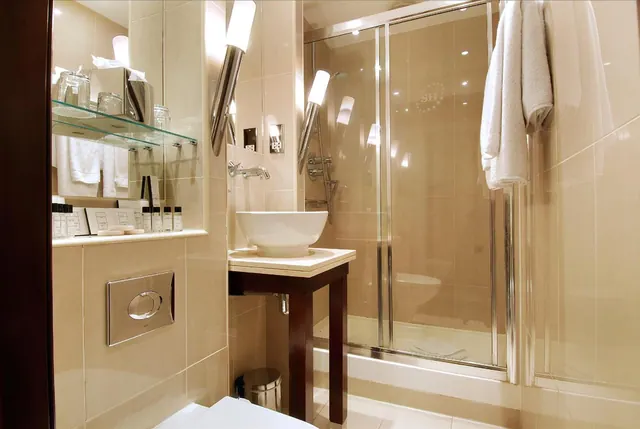 A bathroom with a glass-enclosed walk-in shower, a vessel sink on a wooden stand, wall-mounted lights, and white towels hanging beside the shower.