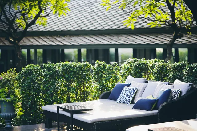 An outdoor daybed with navy and white cushions sits beside a clipped hedge and a tiled pavilion roof.
