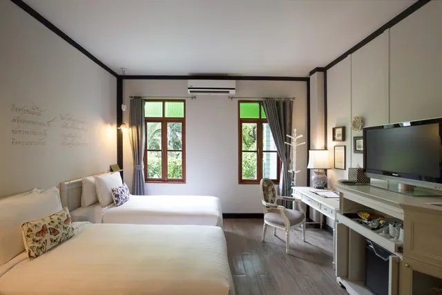 A twin-bedded hotel room with a wall-mounted air conditioner, a writing desk, a television and windows looking out onto trees.