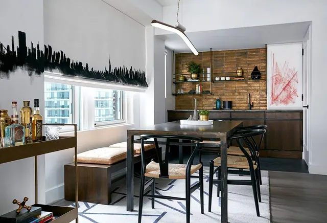 A dining area with a dark wood table, black wishbone chairs, a cushioned bench under the window, a bar cart, and a roller blind printed with a black city skyline.