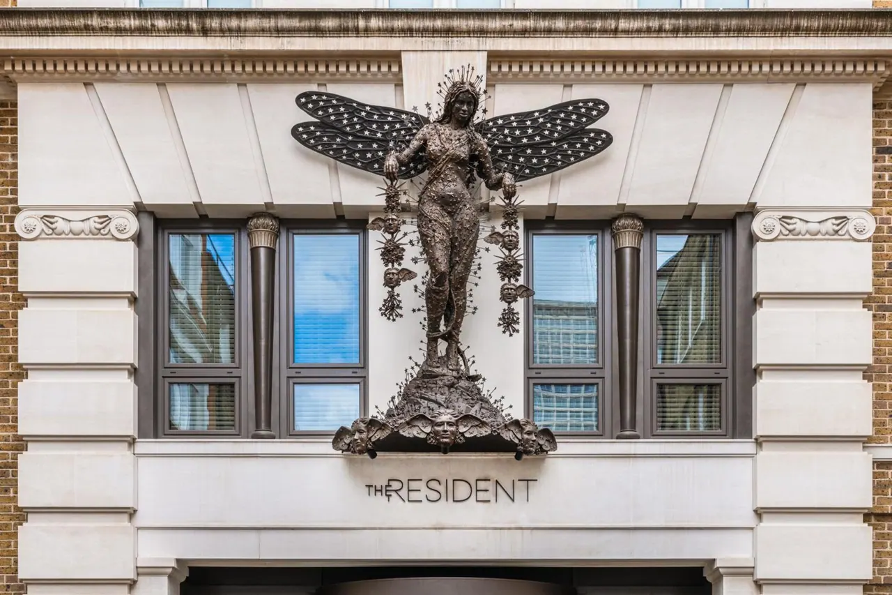 The stone facade of The Resident hotel shows a bronze winged figure statue above the entrance and the hotel name below it.