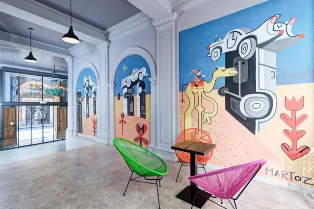 A lobby seating area with colourful woven chairs, a small wooden table and a large painted mural on the wall.