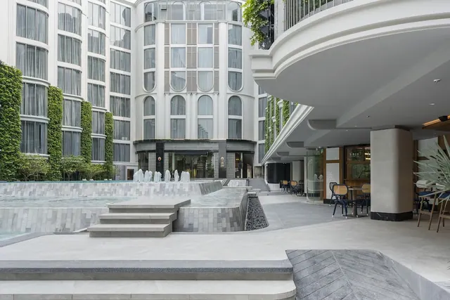 A paved hotel courtyard with a stepped water feature, green wall planting, and an outdoor seating area under a curved overhang.