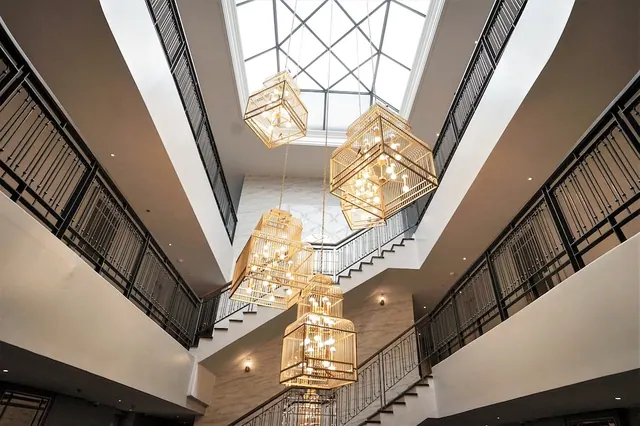 Looking up at a multi-storey atrium with a glass skylight, gold birdcage-style chandeliers hanging above staircases and balcony railings.
