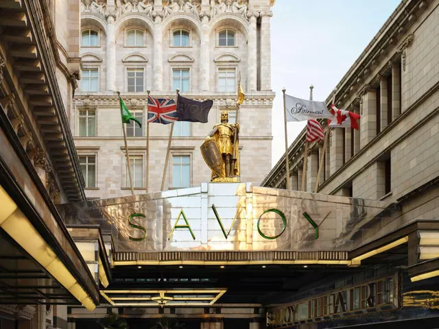 The entrance canopy of The Savoy hotel shows a gold statue above a SAVOY sign, with flags on poles and stone facades behind.