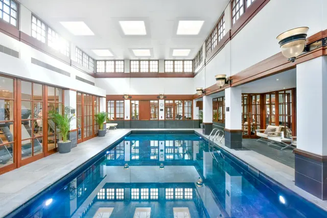 Indoor lap pool with blue water, wood-framed windows, skylights overhead and a seating area to the right.