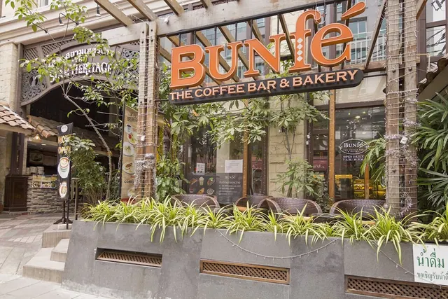 Exterior of the Bunfe coffee bar and bakery storefront with an orange sign, planters and wicker chairs set out on the pavement.