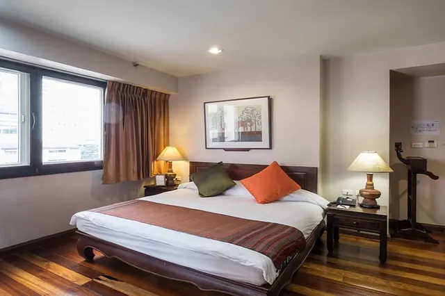 A bedroom with a large bed with a wooden headboard and frame, two bedside lamps, a framed picture on the wall and a window with brown curtains.